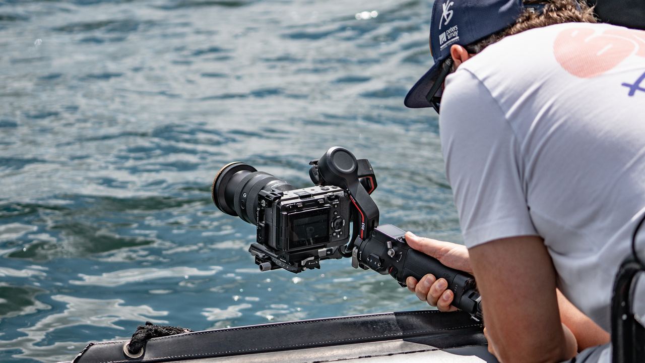 Kamera auf einem Gimbal knapp über dem Wasser, gehalten von einer Person im Boot