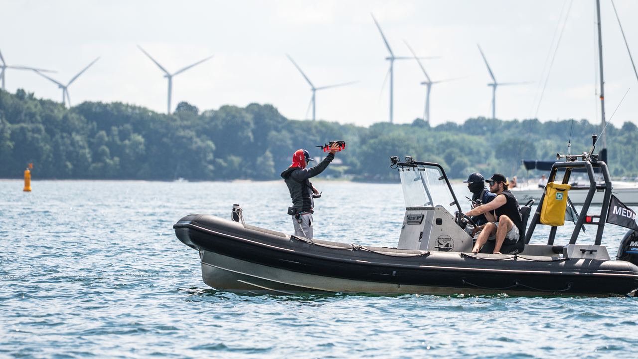 Drohnenstart von Hand aus einem Boot, gelbe Bahnmarke im Hintergrund