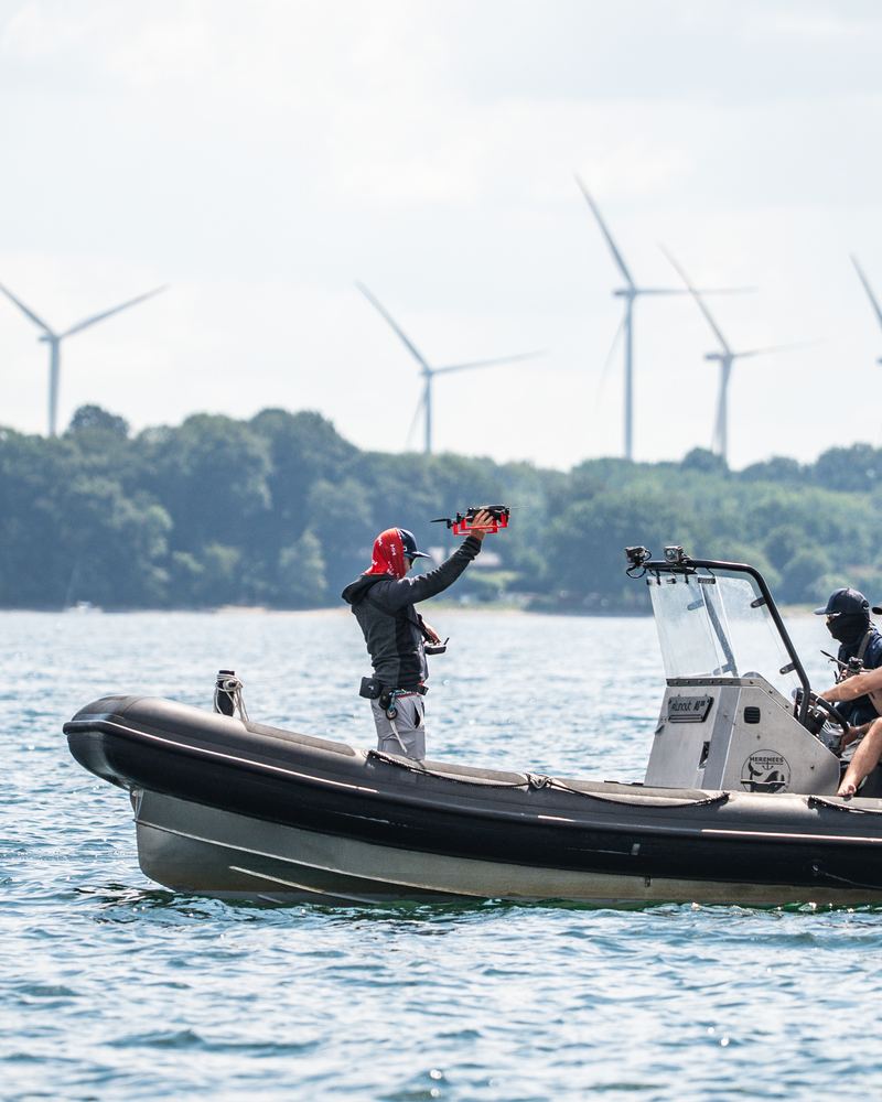 Drohnenstart von Hand aus einem Boot, gelbe Bahnmarke im Hintergrund